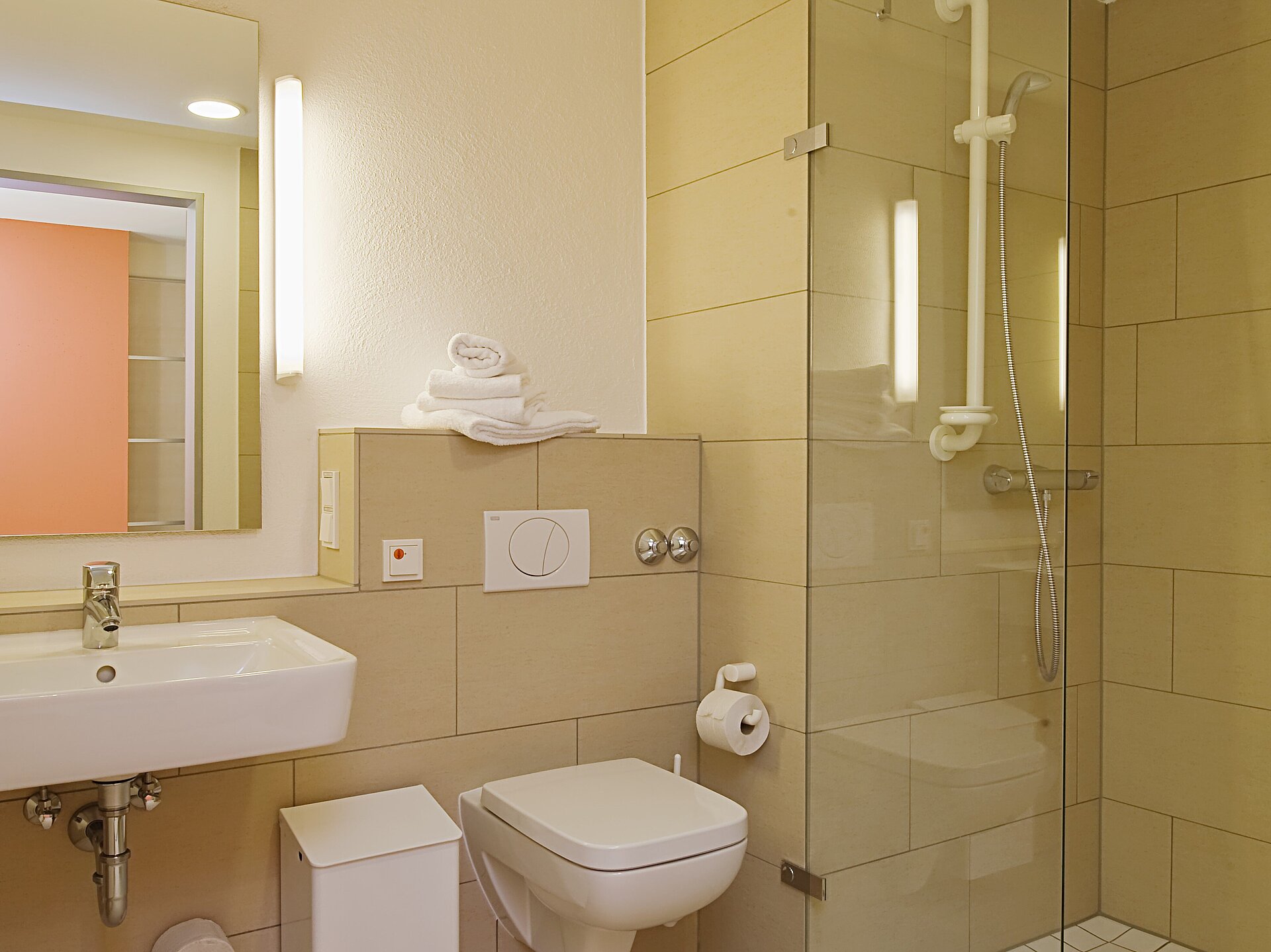 Innenansicht des Badezimmers mit großzügiger Dusche, WC und Waschbecken mit Spiegel.